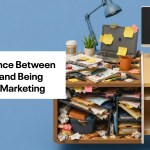A desk covered in sticky notes, balled up papers, pens, coffee cups, notebooks, shelve a lamp and plant. The words, The difference between being busy and being effective in marketing are to the left.
